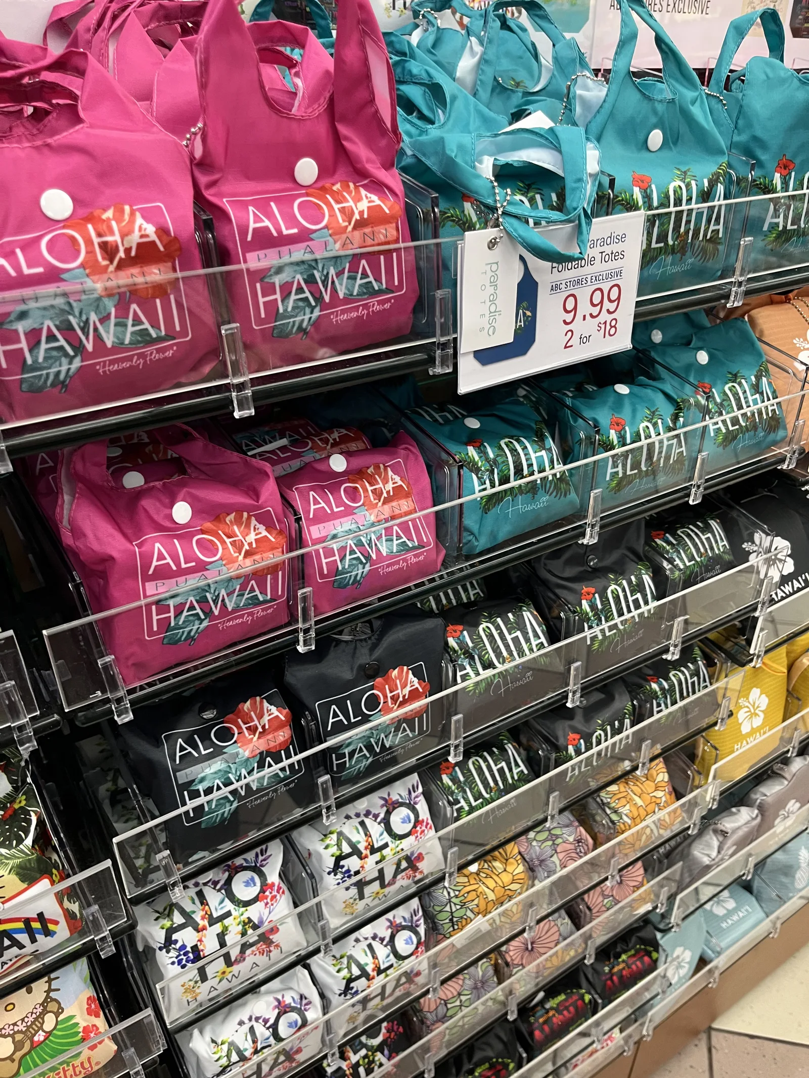 「ALOHA HAWAII」などの文字が入ったピンクや青緑、黒の折りたたみエコバッグが棚に並んでいる