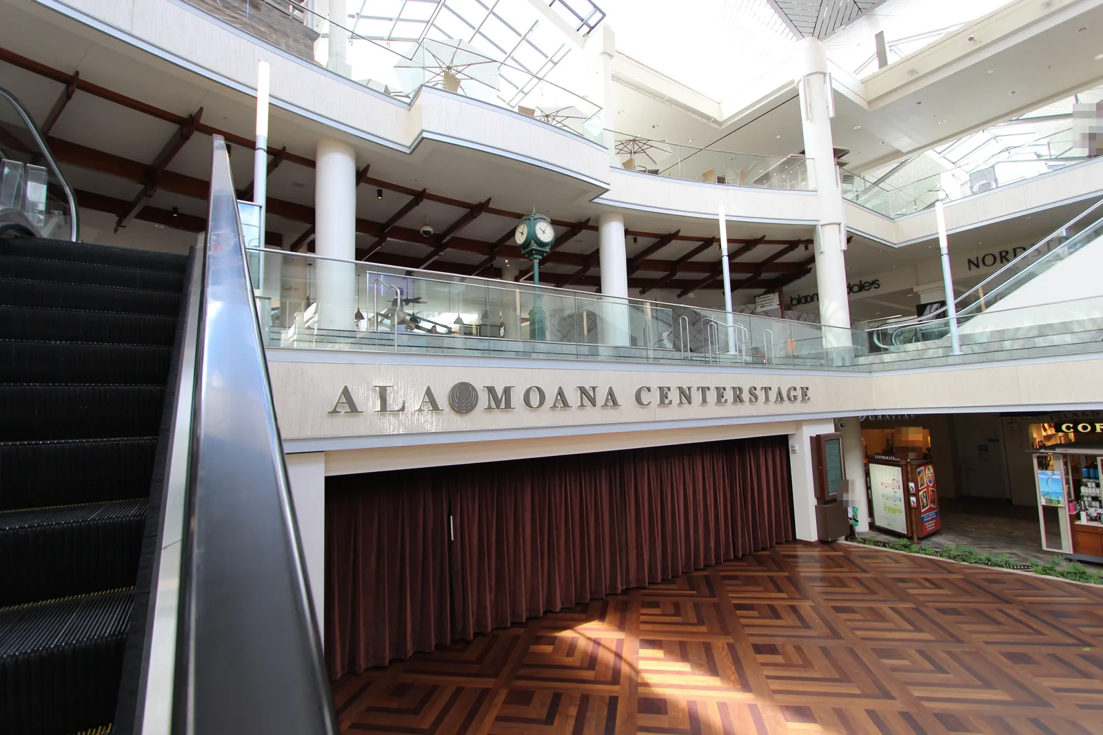 幕の下りたステージの上に「ALA MOANA CENTERSTAGE」の文字。上の階の吹き抜けの奥にブルーミングデールズとノードストロームの看板が見える