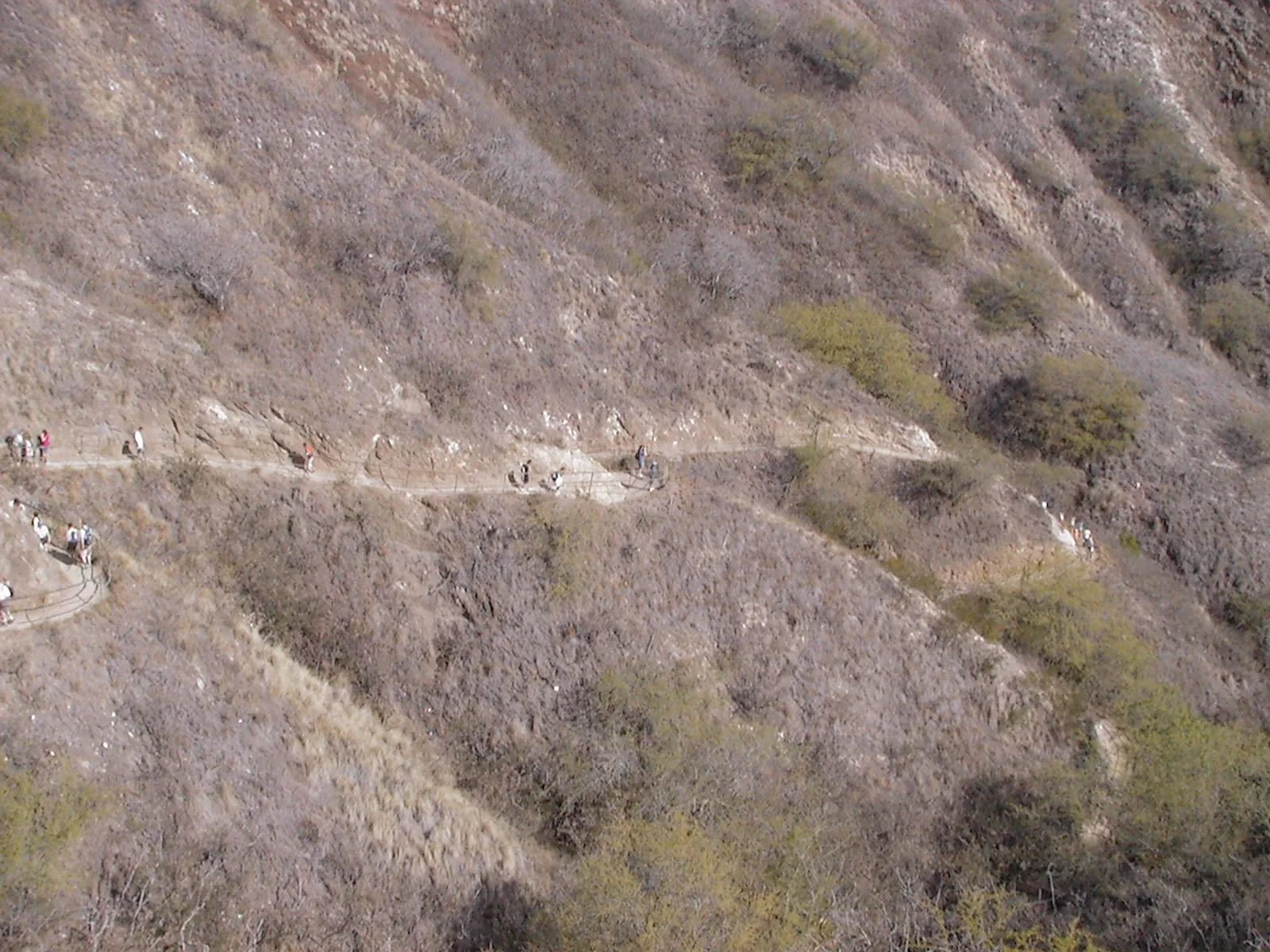 クレーター内側の乾いた斜面を手すりに沿ってジグザグに登る登山道と、歩くハイカーたち