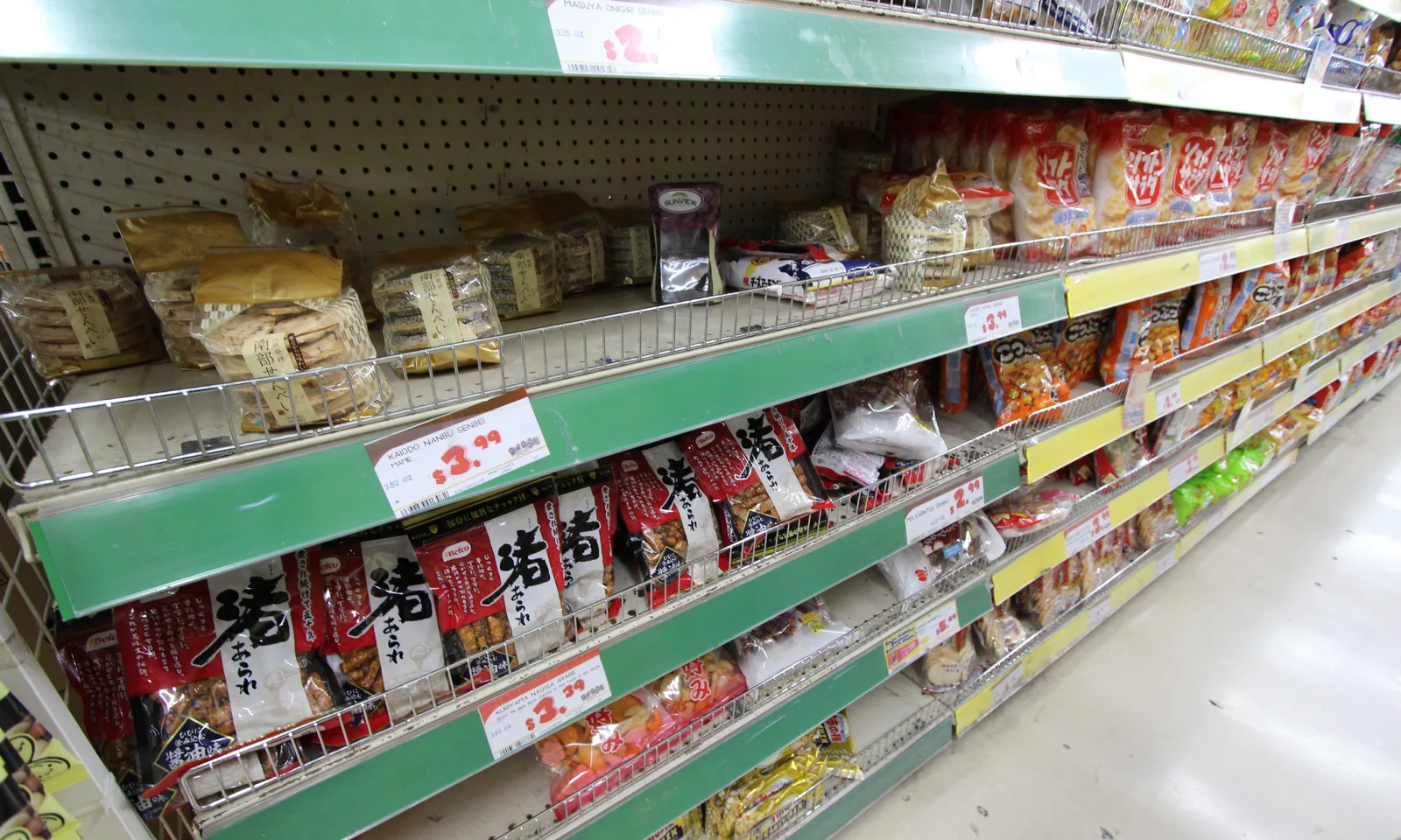 日本のせんべいやあられの袋が並ぶ棚。南部せんべいに3.99ドル、あられに3.39ドルの値札が付いている