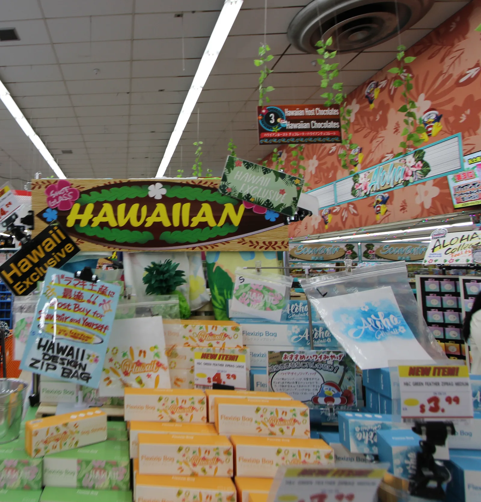 「HAWAIIAN」のサーフボード型の看板の下に、ハワイ柄のジッパーバッグの箱が並び、3.99ドルの値札が付いている