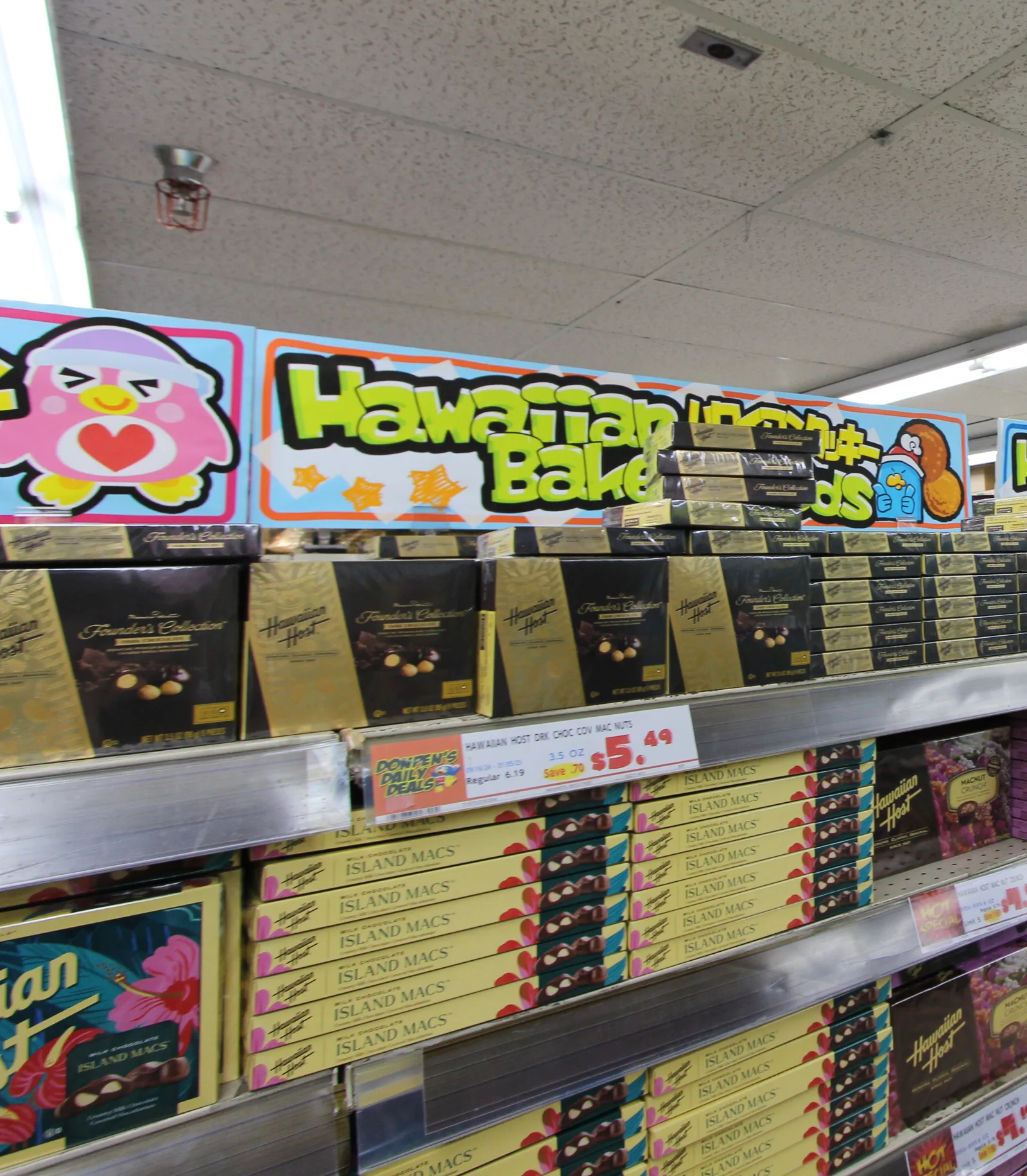 「Hawaiian Baked Goods」の看板の下に、ハワイアンホーストの金色の箱と「ISLAND MACS」の箱が並び、5.49ドルの値札が付いている
