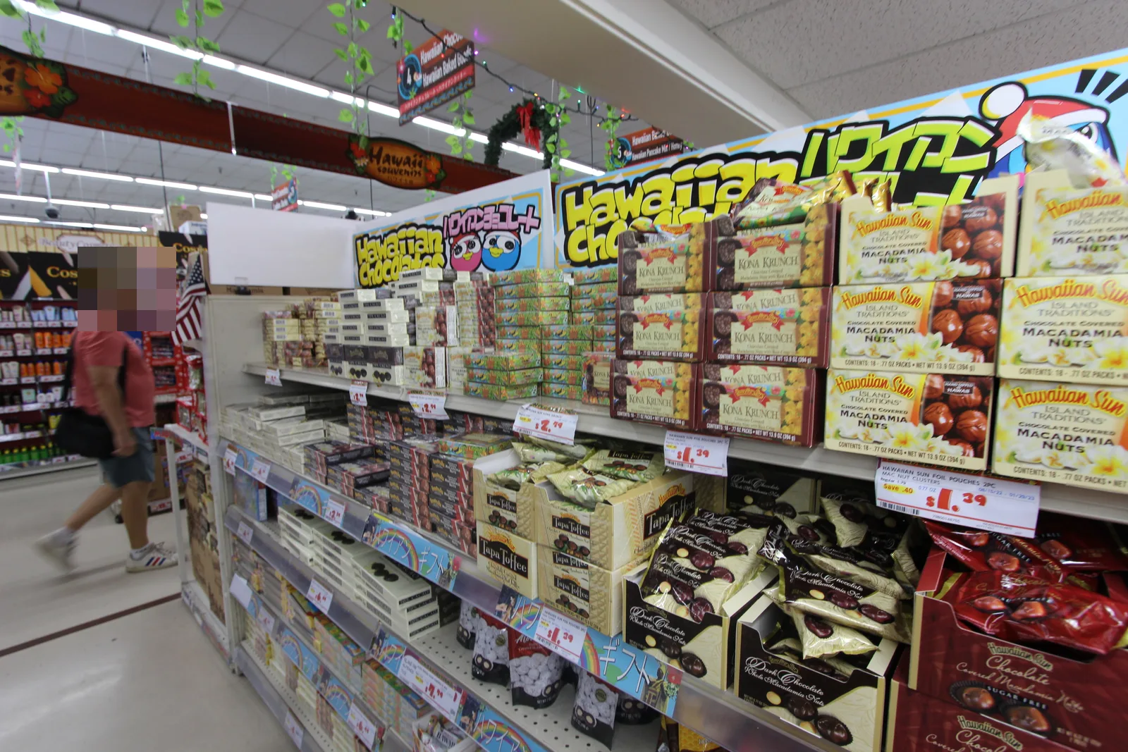「Hawaiian Chocolates」の看板の下に、ハワイアンサンのマカダミアナッツチョコや「KONA KRUNCH」の箱が並ぶ棚