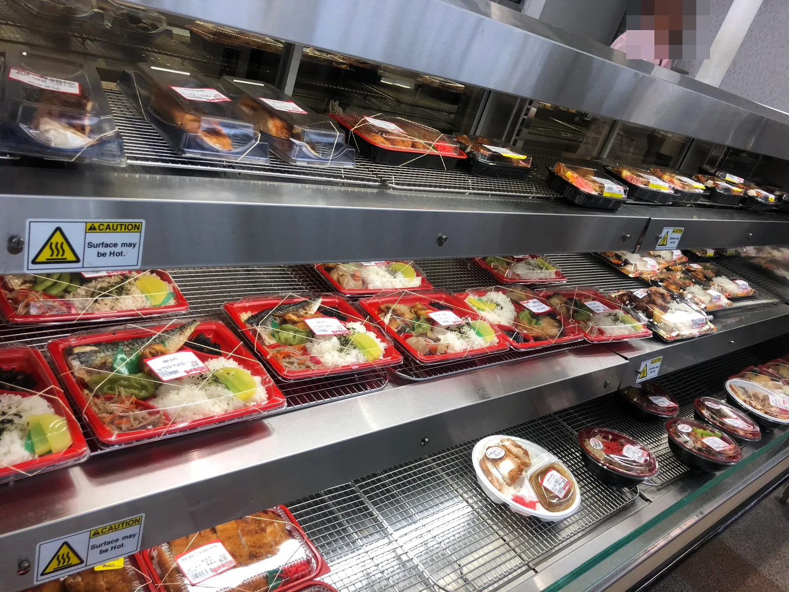 保温ケースに、焼き魚や煮物が入った赤い容器のお弁当や、とんかつの丼が並ぶ