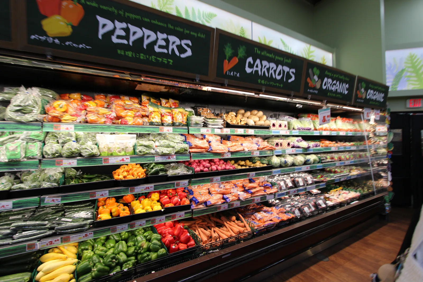 「PEPPERS」「CARROTS」「ORGANIC」の看板の下に、パプリカやにんじん、葉物野菜が並ぶ冷蔵棚