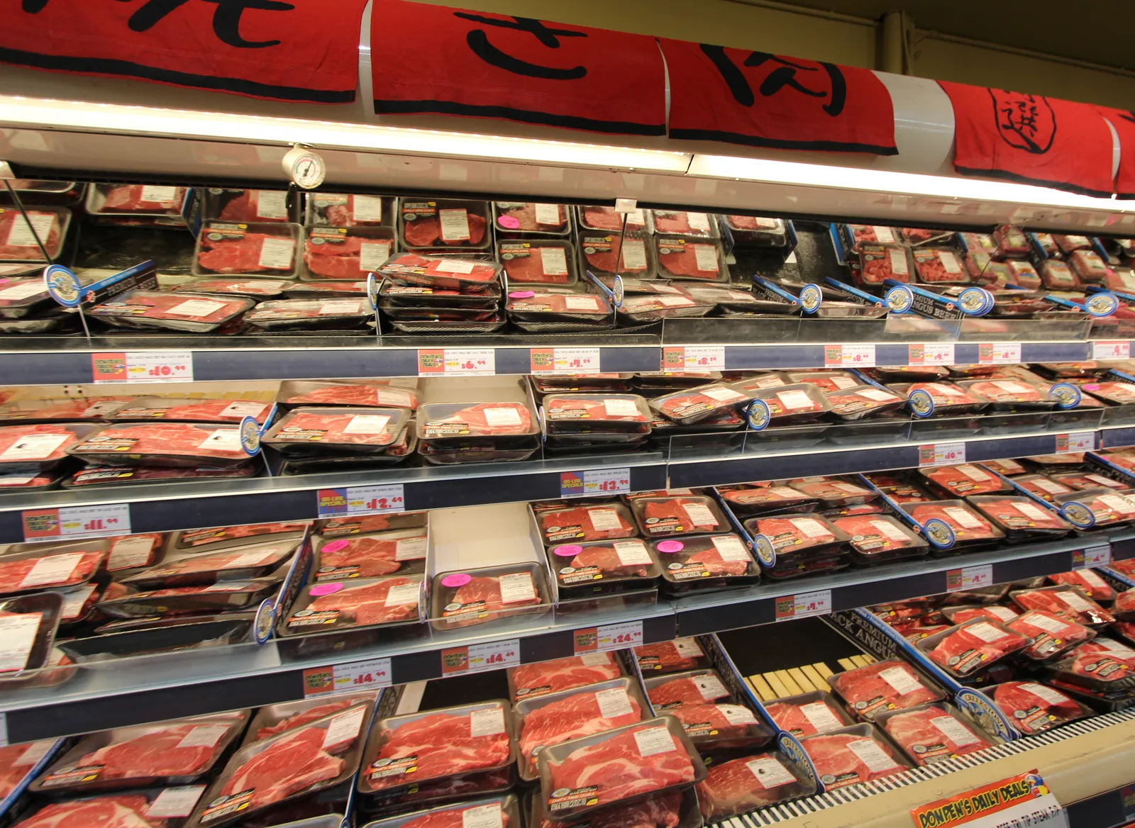 赤い暖簾の下のケースに、ステーキ用などの牛肉のパックがぎっしり並んでいる