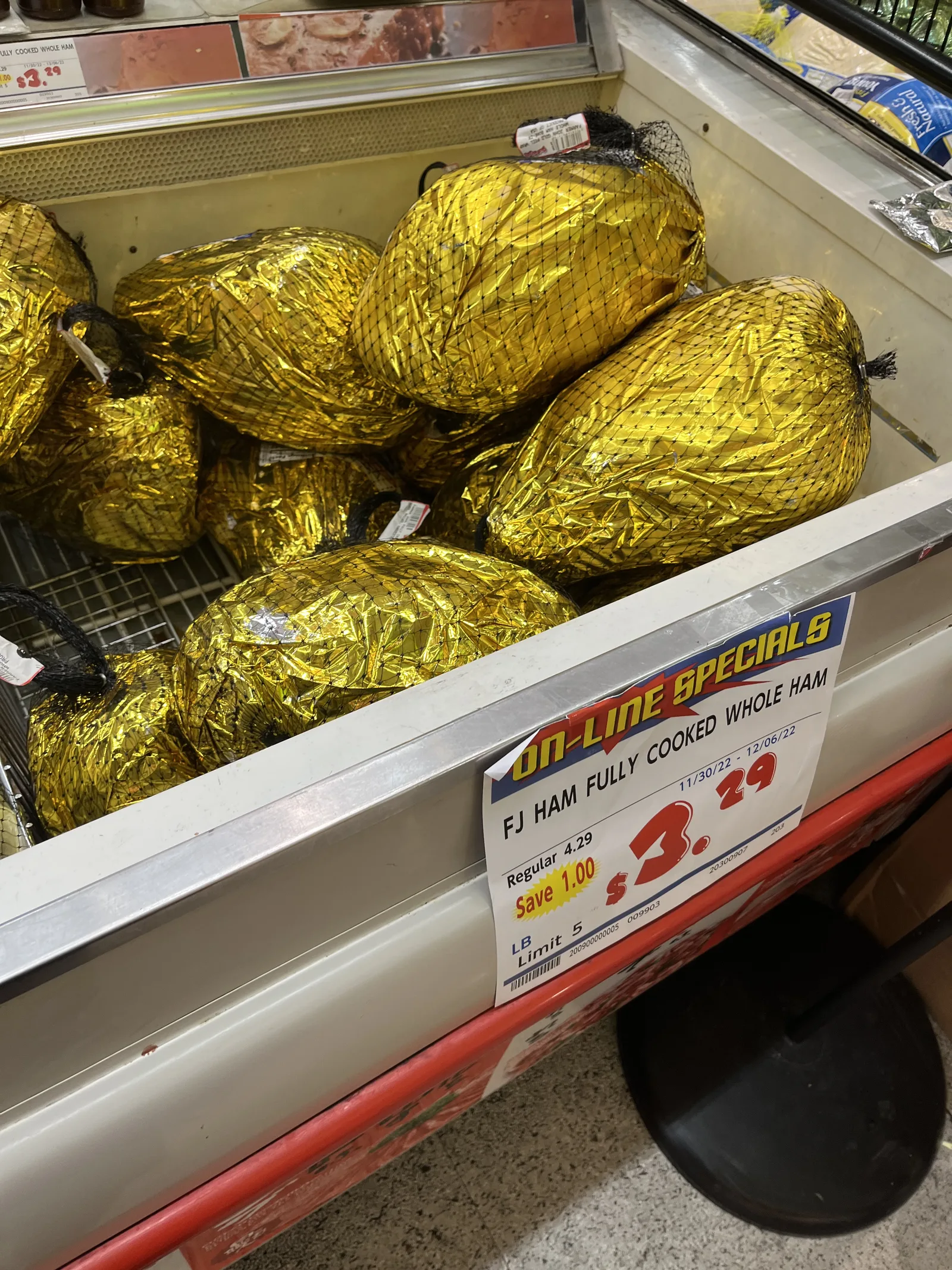 冷蔵ケースに金色の包みのハムが積まれ、「ON-LINE SPECIALS」の札に1ポンド3.29ドル(通常4.29ドル)と書かれている