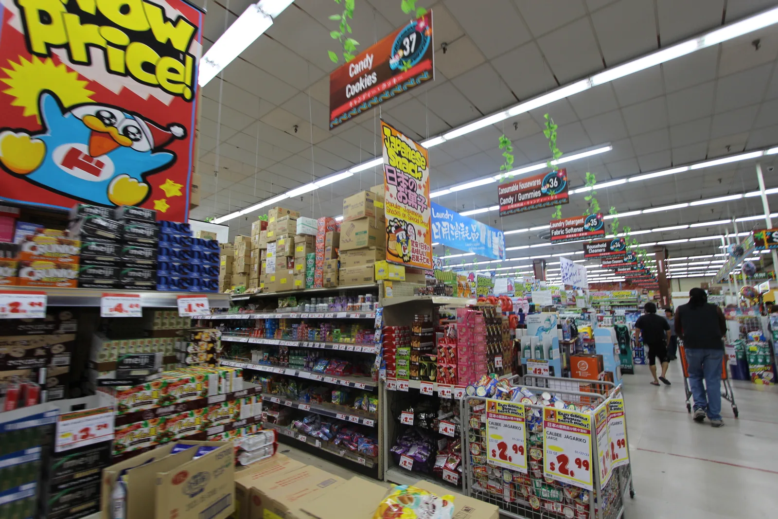 大きなドンペンの「Wow Price!」の看板の下に、お菓子の箱や2.99ドルのスナックのワゴンが並ぶ