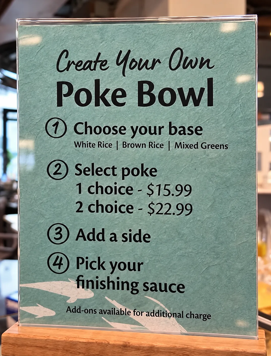 木の台に立てられた緑色の案内板。「Create Your Own Poke Bowl」の見出しの下に、ベース・ポケ・サイド・ソースを選ぶ4つの手順が書かれている