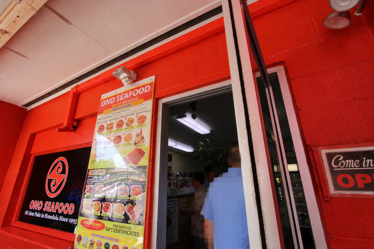 赤い壁のオノシーフードの入口。窓に店名のロゴ、入口の横にポケとポケ丼の写真付きメニューが貼られている