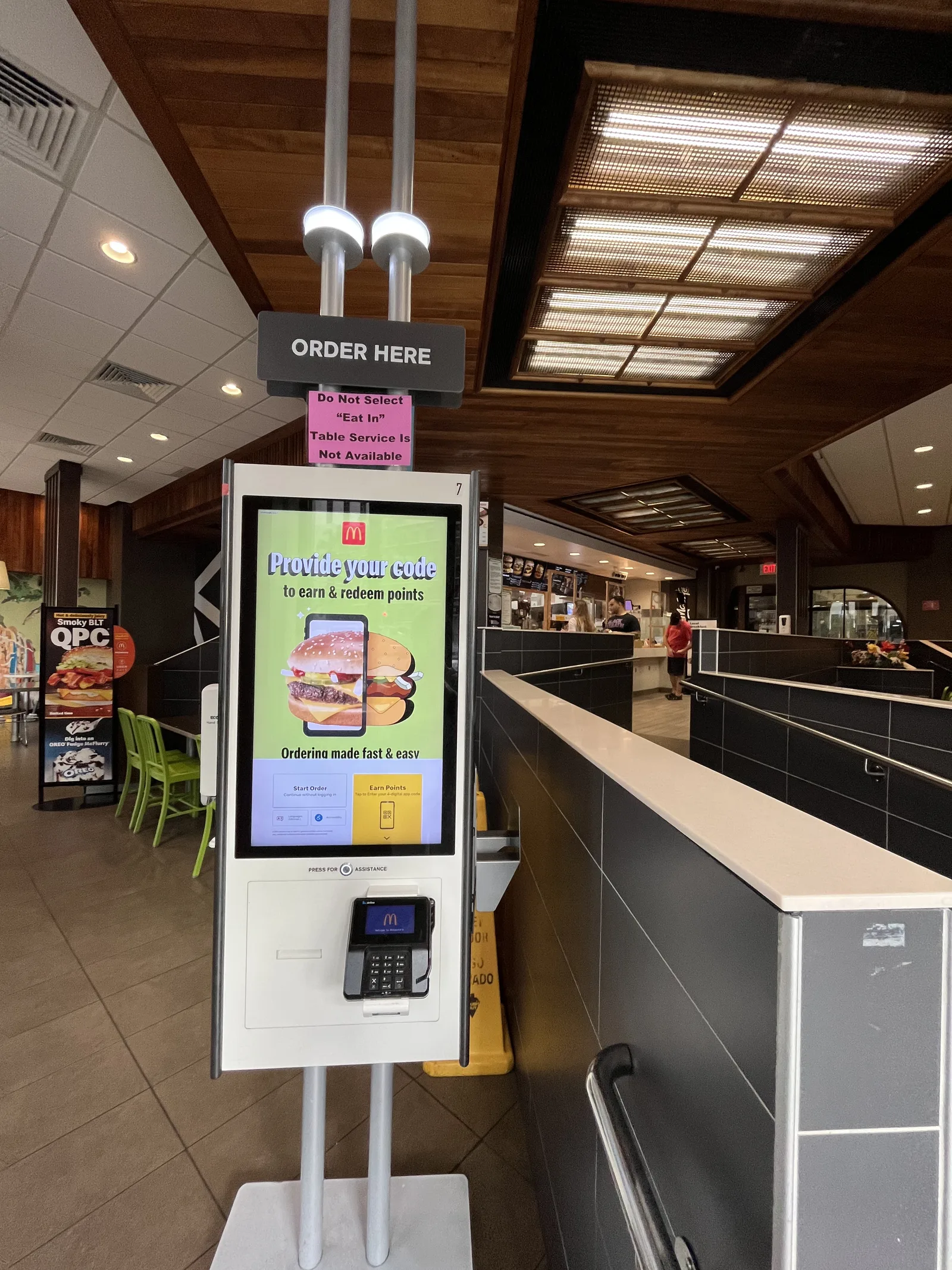 ハワイのマクドナルドの店内に立つ「ORDER HERE」の注文用タッチパネル。上に「Eat Inを選ばないで、テーブルサービスはありません」という張り紙がある