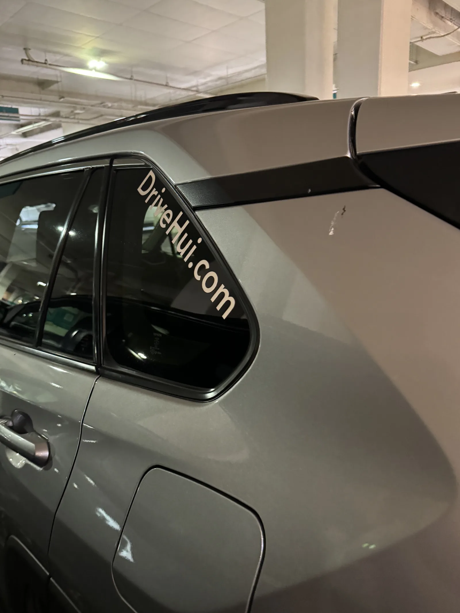 立体駐車場に停まっているシルバーのSUV。後ろの窓に「DriveHui.com」の白い文字が貼られている