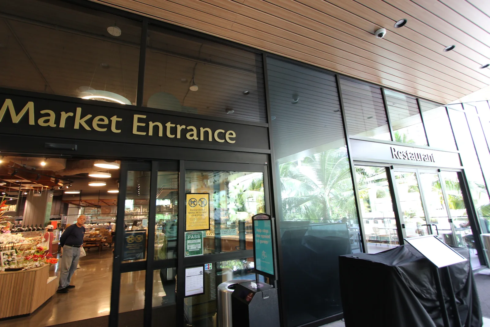 「Market Entrance」の看板が掛かったワイキキ・マーケットのガラス張りの入口。奥にお惣菜のケースが見える