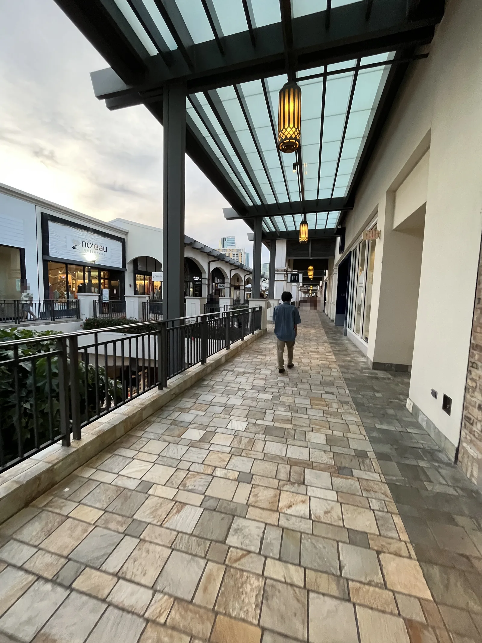 ガラスの屋根がかかった石畳の屋外通路。片側にお店が並び、奥へ通路が続いている