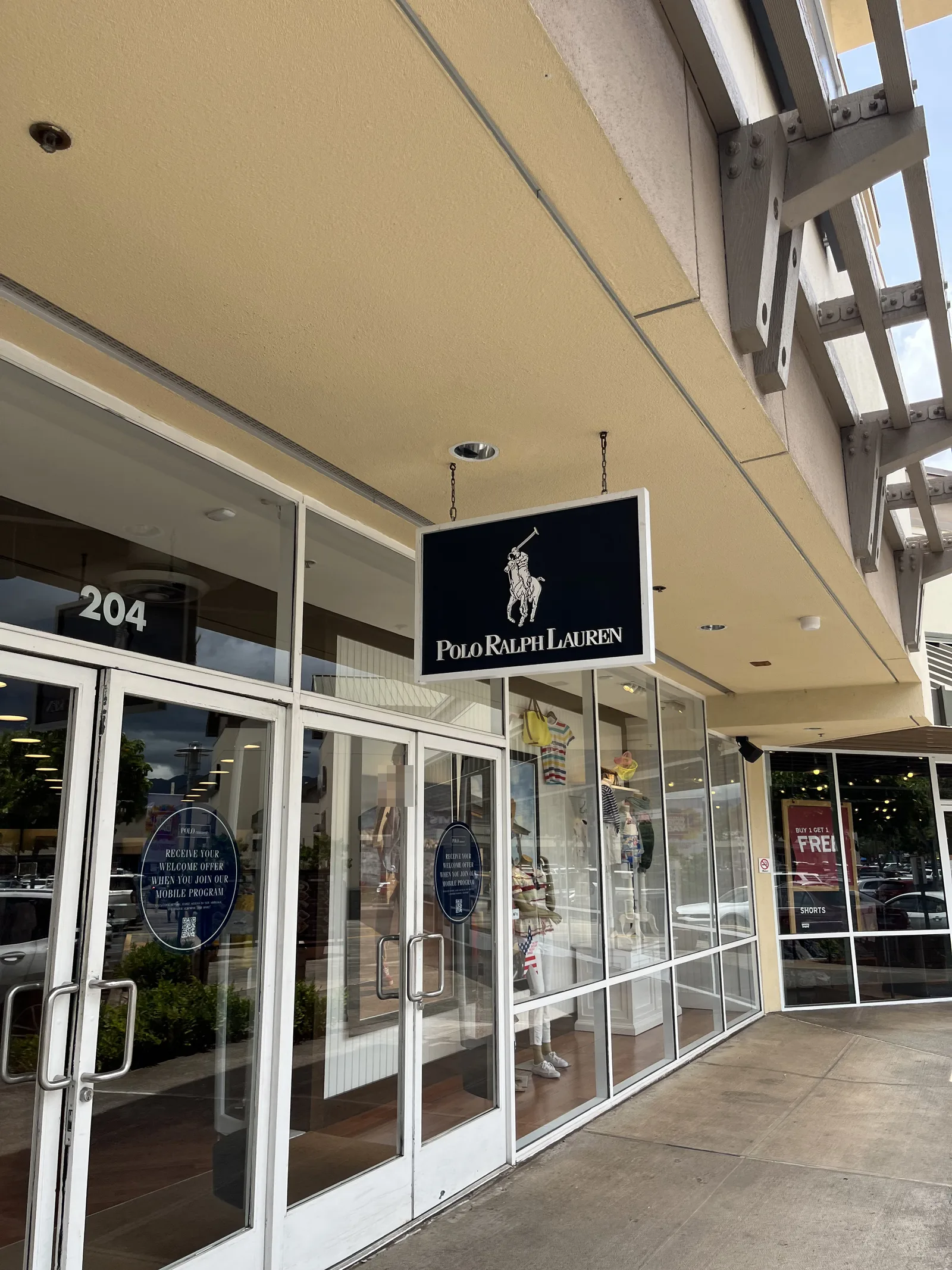 屋外の通路に面したポロ ラルフ ローレンの店舗。紺色の吊り看板とガラス張りの入口