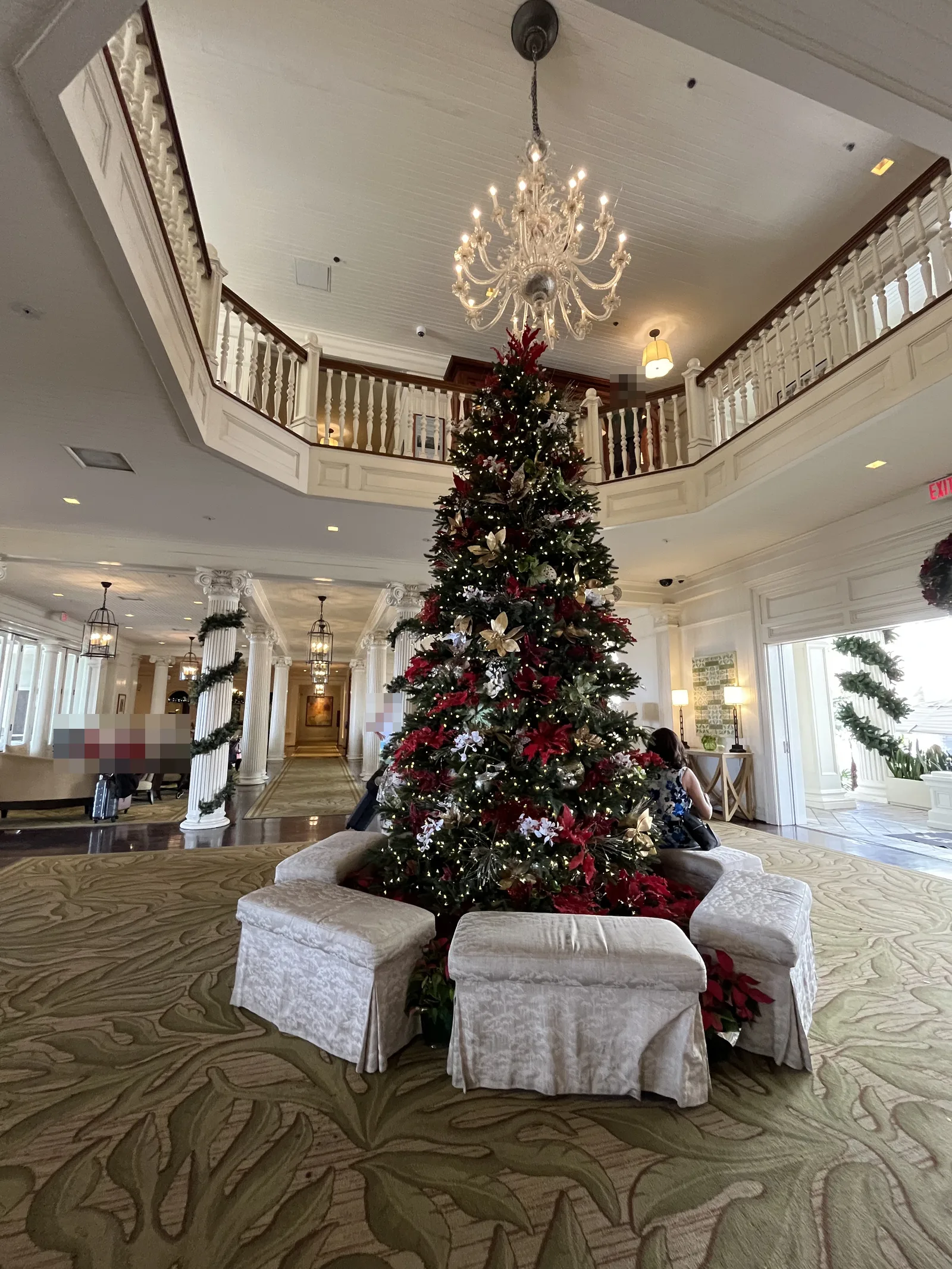 2階まで吹き抜けの本館ロビー。白い回廊とシャンデリアの下に大きなクリスマスツリーがあり、周りを白いスツールが囲む