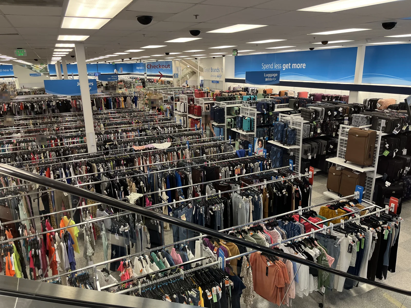 広い売り場に服のラックが何列も並び、右手にスーツケースの棚がある。売り場の案内板には英語と日本語で「Luggage 旅行カバン」と書かれている