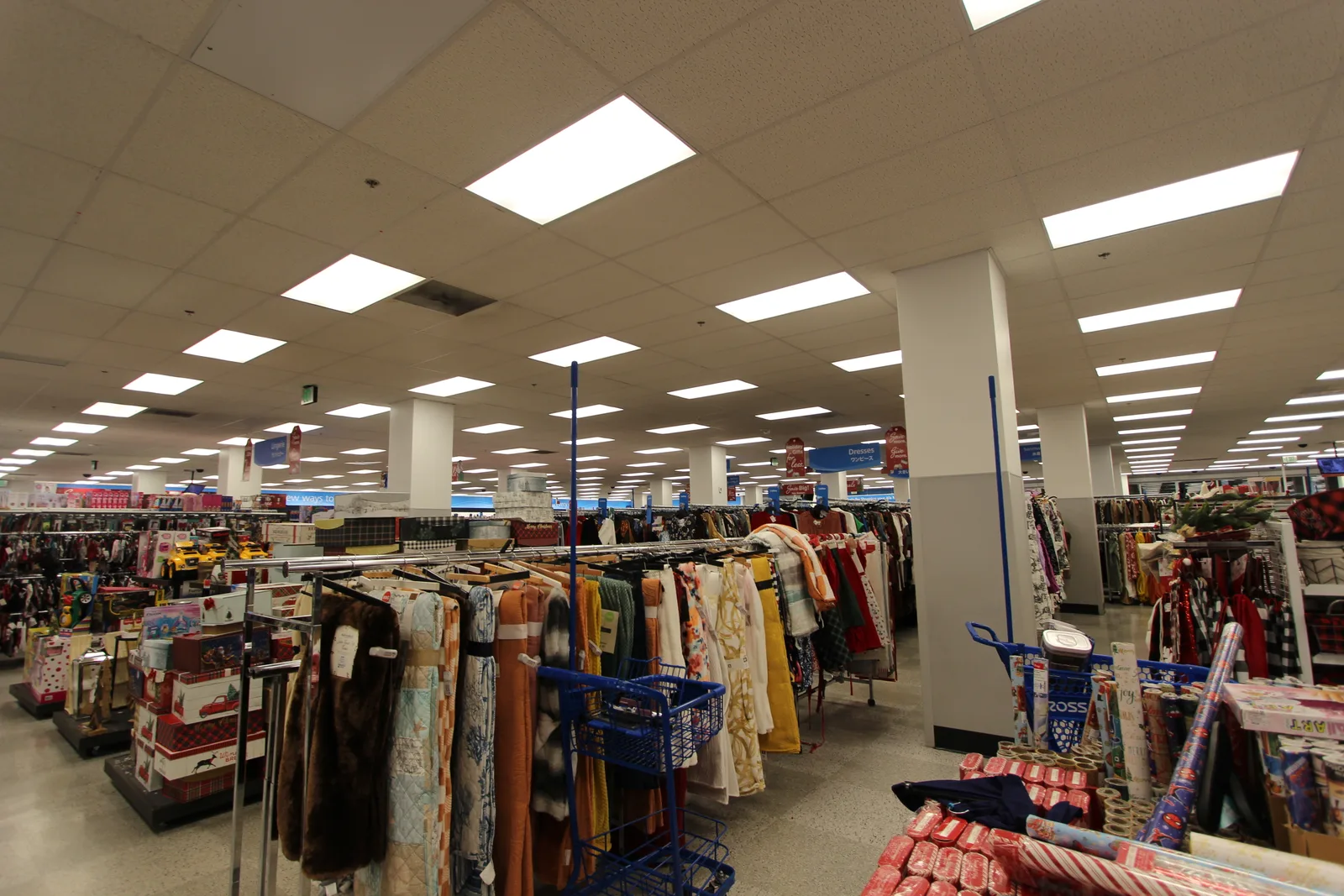 広い売り場に服のラックや棚が奥まで続き、手前にクリスマスの包装紙やギフトボックス、青い買い物カートが並んでいる
