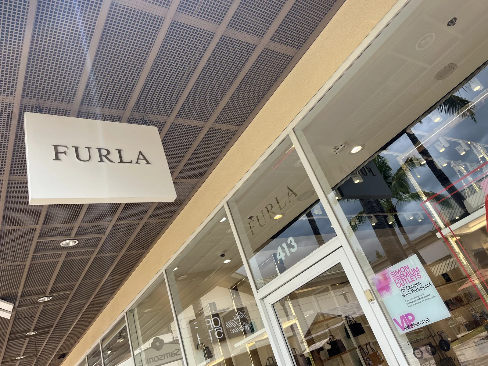「FURLA」の看板の店舗の入口に、ピンクの「SIMON PREMIUM OUTLETS VIP Coupon Book Participant」のステッカーが貼られている