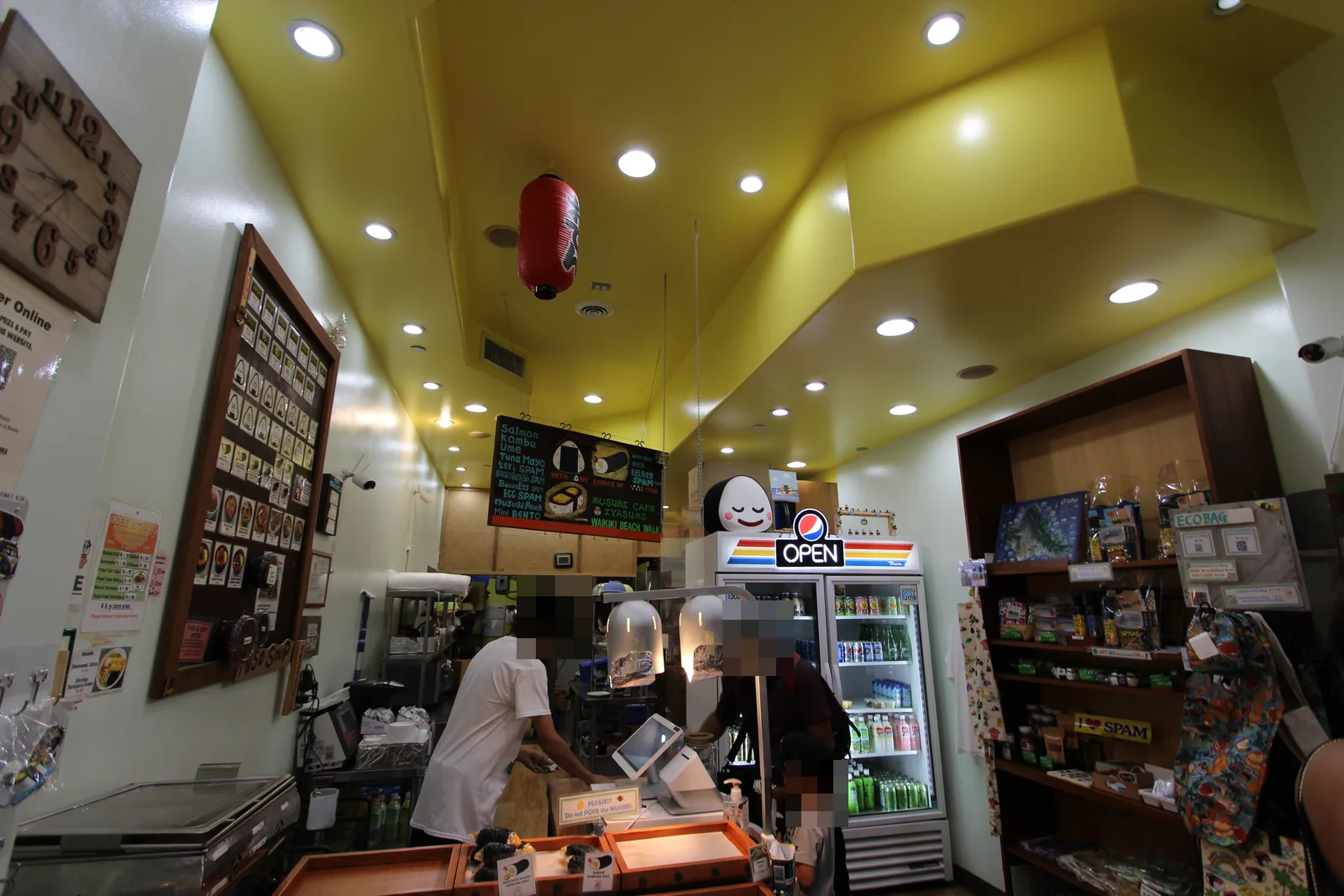 黄色い天井の小さな店内。むすびの名前が並ぶ黒板メニューとおにぎりのキャラクター、レジと飲み物の冷蔵ケース