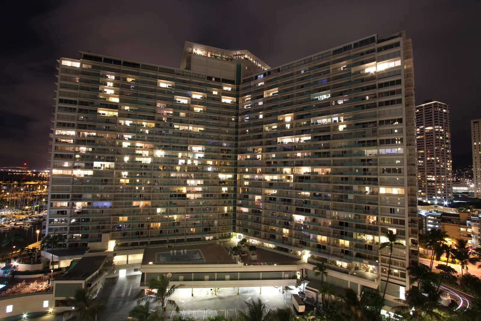夜のイリカイ ホテル。V字形に広がる高層の建物の窓に明かりがともり、左奥にヨットハーバーが見える