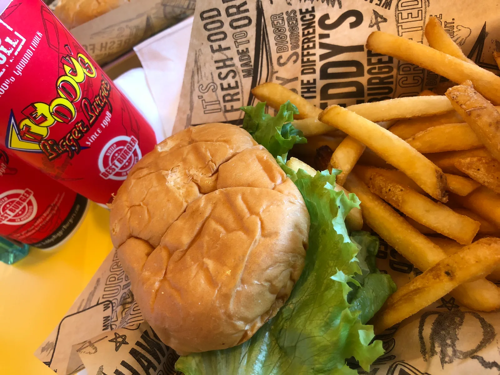 紙を敷いたトレーにのったバーガーとフライドポテト、赤いロゴのカップ